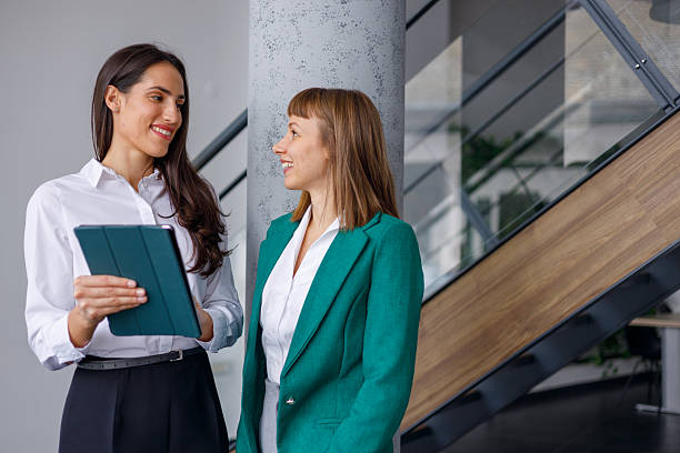 istock Two smiling businesswomen collaborating in modern office, discussing data on digital tablet during a work meeting 2241233049