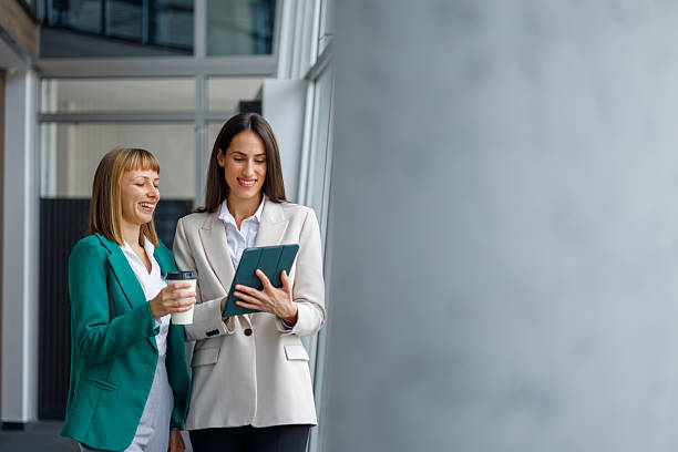 istock Businesswomen walking through office corridor, smiling and discussing project on digital tablet 2241235357