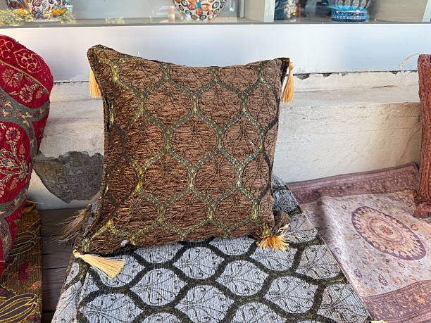 istock Brown decorative pillow with tassels placed on patterned textiles in outdoor display. Craft, tradition, and interior decoration in cultural textile heritage. 2241237505