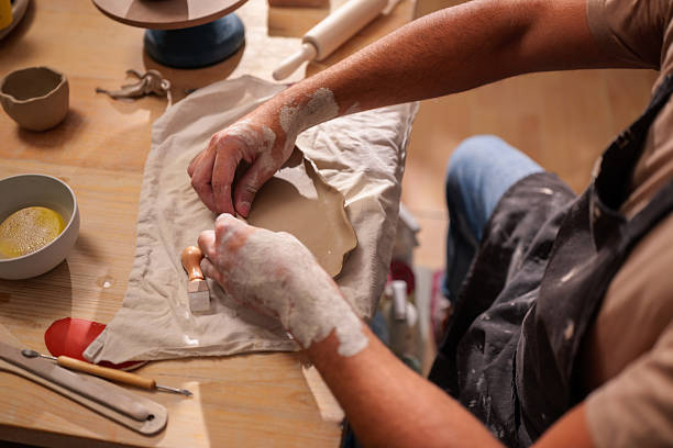 istock Ceramist is working on a clay plate, imprinting a decoration using a wooden stamp, surrounded by tools and materials in a pottery workshop 2241237704