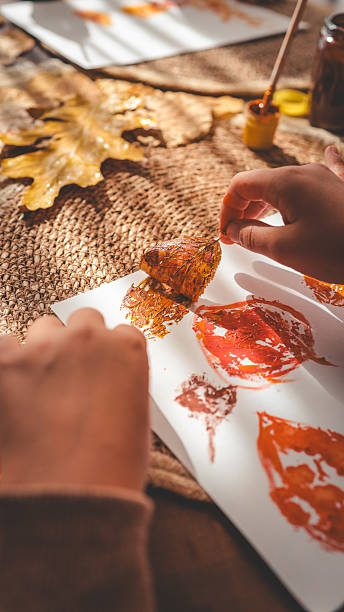 istock Child's hand painting leaf prints on paper 2241239401