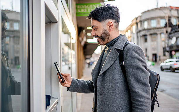 istock Man using smartphone for mobile payment at city atm 2241242622