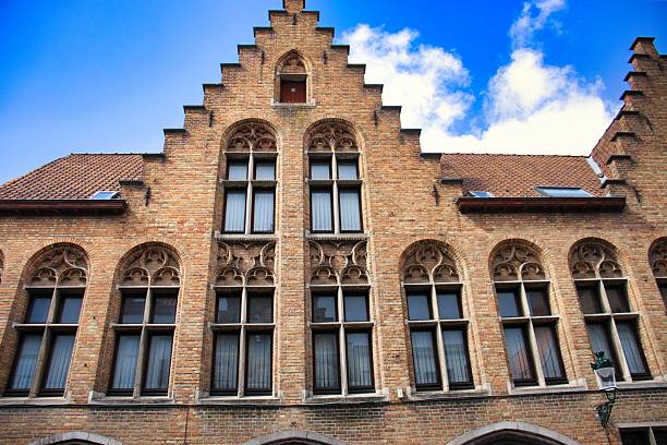Majestic medieval brick building with ornate architecture and gabled roofline set against a vibrant blue sky with fluffy clouds.
