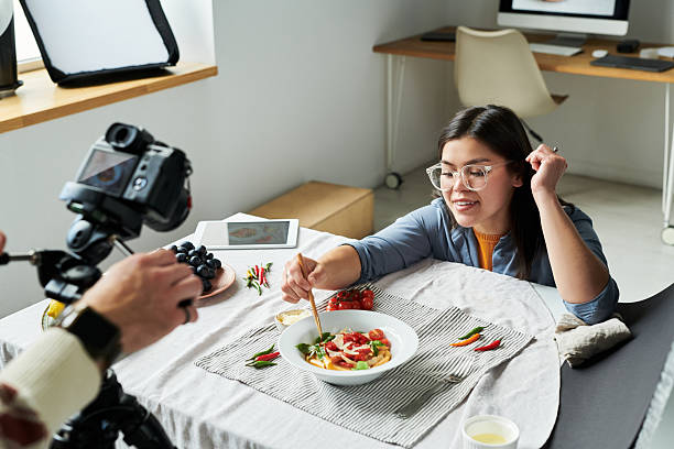 istock Asian Woman Eating Salad While Being Filmed in Modern Kitchen 2241245406