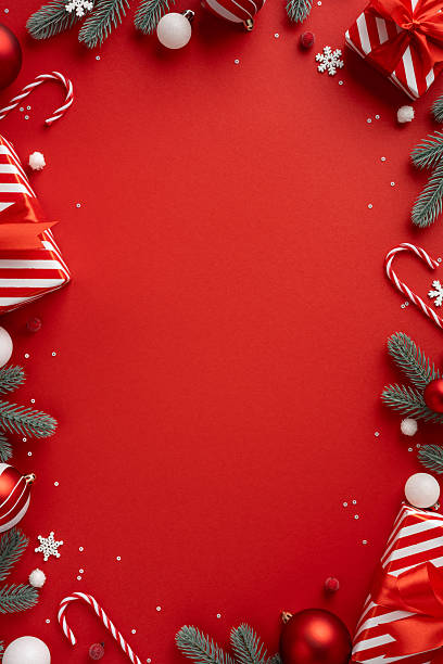 istock Vertical holiday scene with a bold red backdrop framed by evergreen branches, striped gift boxes, candy canes, baubles and snowflakes ready for Christmas and New Year greetings 2241245859