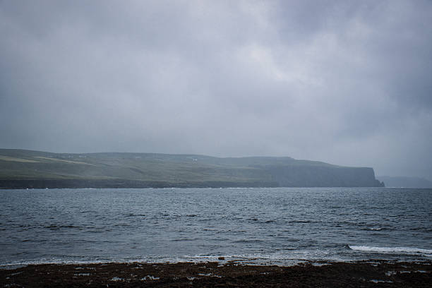 Serene, moody seascape with rolling hills and dramatic cliffs under an overcast sky.