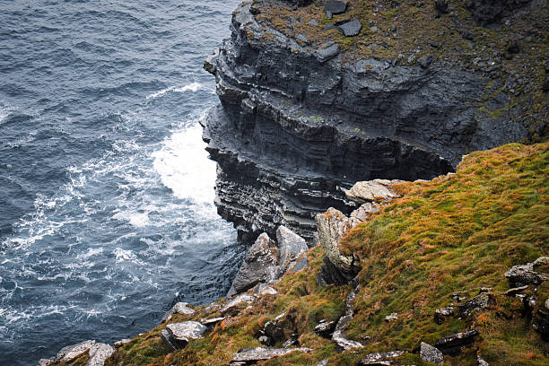 Dramatic sea cliffs overlooking the churning ocean, covered in lush green moss and weathered rock formations.