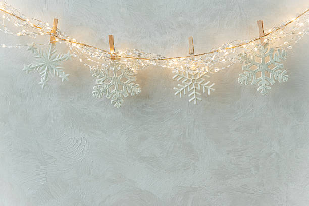 istock White Snowflake Ornaments Hanging on String Lights Against Textured Wall 2241252221