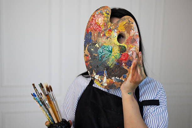 istock Female painter hiding face behind colorful palette in art studio 2241252372