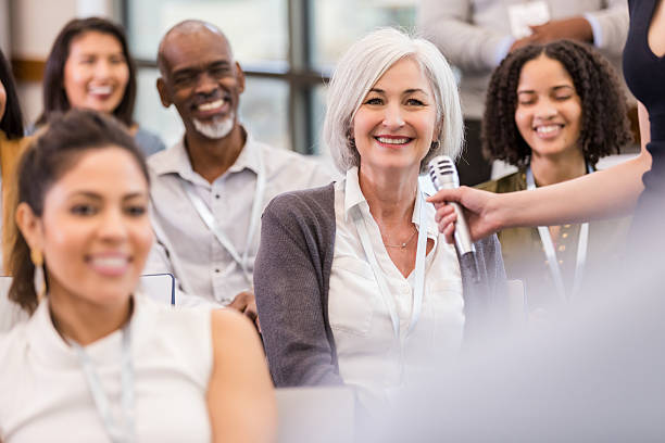 istock Diverse group of people at a conference, smiling and engaged with a speaker holding a microphone. 2241257306