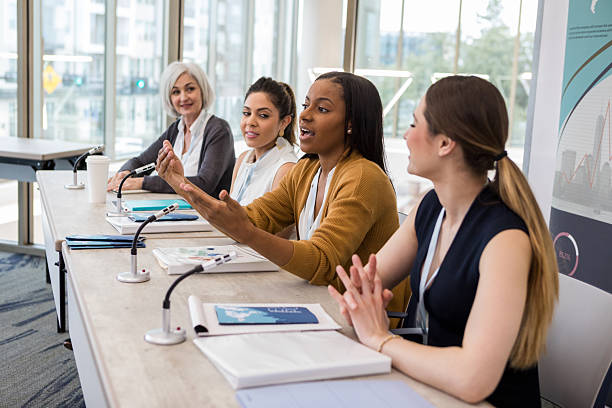 istock Diverse women engage in discussion at a panel event with microphones and documents. 2241257317