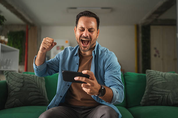 istock Man winning mobile game celebrating victory on couch 2241259448