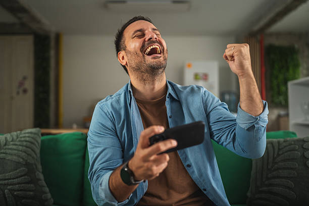 istock Man winning mobile game celebrating victory on couch 2241259542