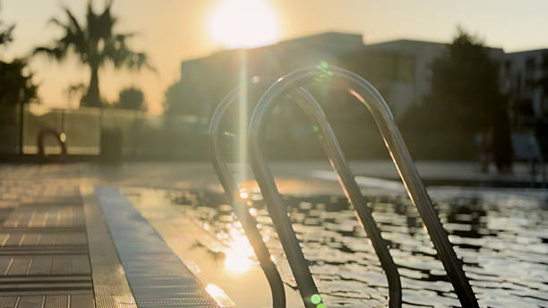 A peaceful and visually striking scene featuring a pool railing silhouetted against the warm glow of sunset. The golden hour light reflects gently off the still water, casting soft shadows and creating a calm, almost meditative atmosphere. The combination of architectural lines and natural light makes this a perfect visual for themes of relaxation, summer evenings, luxury lifestyle, and tranquil outdoor spaces. Ideal for travel brochures, wellness content, and serene visual storytelling.