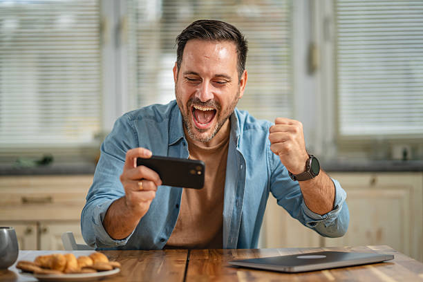 istock Happy man playing mobile game on smart phone at home 2241260950