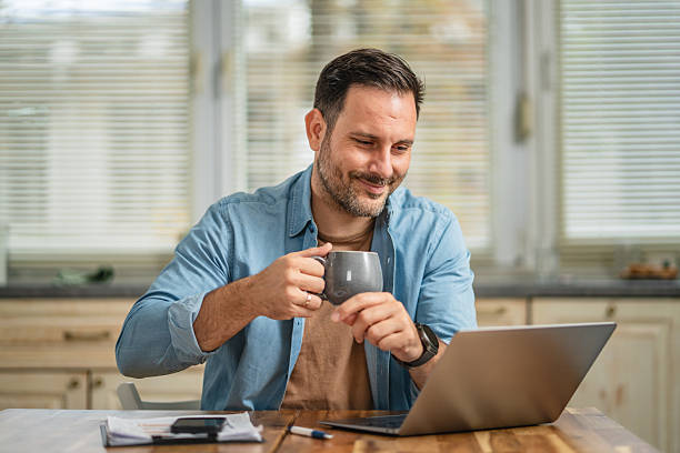 istock Man drinking coffee working from home on laptop 2241261601