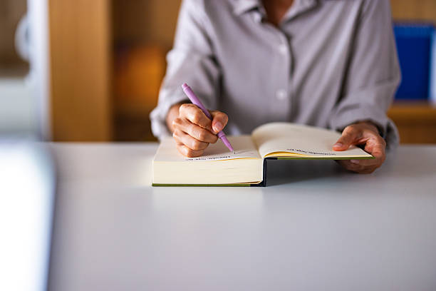 istock Person Writing in Open Book With Pink Pen at Desk During Study Session 2241263772