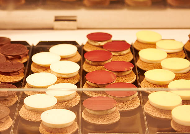 Colorful assortment of dessert treats arranged in a bakery display, featuring round chocolate and cream toppings on biscuit bases, highlighting diverse flavors and inviting textures for enthusiasts