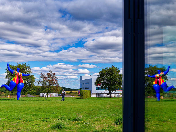 Künzelsau, Germany - August 31, 2025: Public sculpture garden of the Museum Würth 2 in Künzelsau on a summer's day. Visitors view at the colorful Nana sculpture by artist Niki de Saint Phalle. The sculpture is reflected in a windowpane