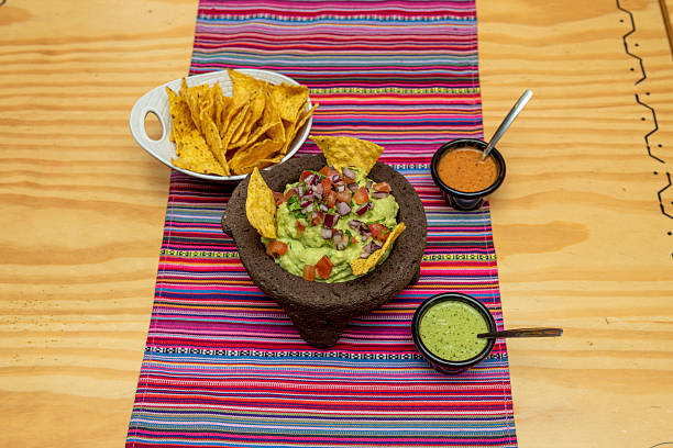 istock Mexican volcanic stone molcajete filled with guacamole with corn chips, cheese sauce and hot sauce with pico de gallo 2241266835