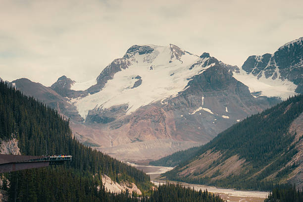 istock Scenic mountain range with snow-capped peaks, evergreen trees, and river 2241267639