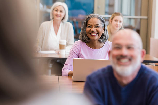 istock Diverse group of smiling adults engaging in a learning environment, some with laptops. 2241269793