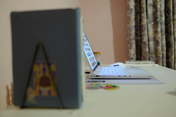 A laptop and books are on a white desk. Also, there is a notebook standing on the desk.