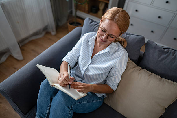 istock Woman writing in journal on couch at home 2241272850