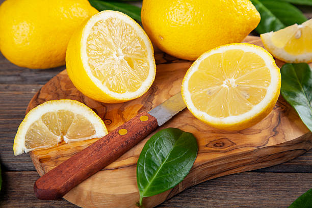 Fresh and ripe lemons with leaves on olive cutting board on brown rustic wooden table.