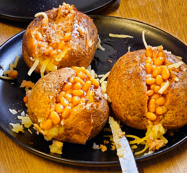 Jacket potetoes with beans for three people Nottingham, England, December 21, 2024. An excellent and hearty, typically English dish. These are jacket potatoes, whole potatoes baked in the oven with the peel and then stuffed. In the photo, the potato is cut in half and topped with tuna, beans, and thinly sliced cheddar cheese. tuna jacket potato stock pictures, royalty-free photos & images