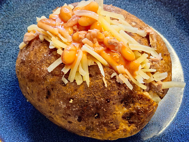 A jacket potato also stuffed with cheddar cheese Nottingham, England, December 21, 2024. An excellent and hearty, typically English dish. These are jacket potatoes, whole potatoes baked in the oven with the peel and then stuffed. In the photo, the potato is cut in half and topped with tuna, beans, and thinly sliced cheddar cheese. tuna jacket potato stock pictures, royalty-free photos & images