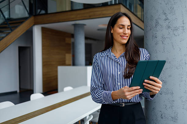 istock Businesswoman standing in modern office using digital tablet, smiling and connecting online, planning strategy 2241283403