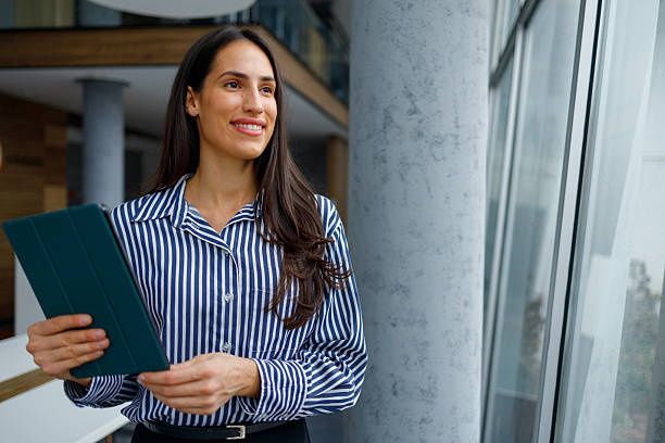 istock Young businesswoman smiling, standing with tablet in modern office, thinking about future business strategy 2241283554