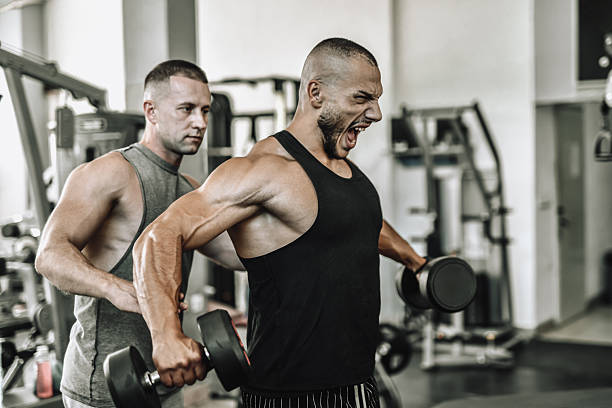 istock Strong Man Lifting Dumbbells with Spotter in Indoor Gym During Intense Workout Session 2241283566