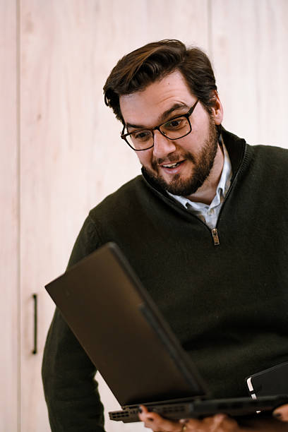 istock Man in a sweater smiles while looking at his laptop in a cozy indoor setting during a remote work session 2241286677
