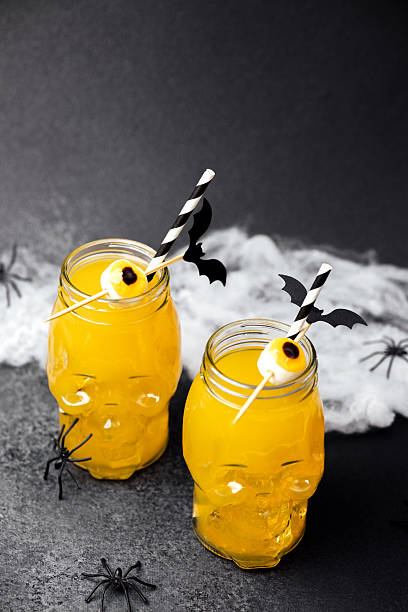 istock Two yellow spooky drinks in skull jars with candy eyes and bat decorations on a dark background 2241287234