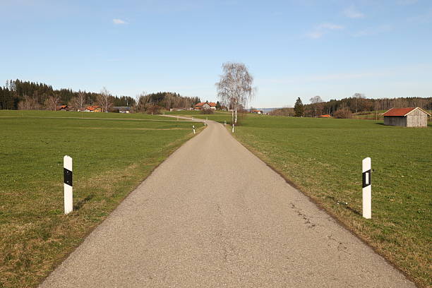 A road with a few houses in the background. The road is empty and there are no cars on it