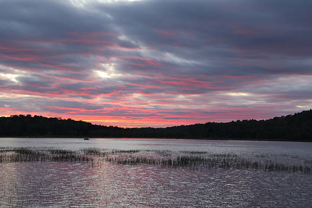 A panoramic view of a lake in the Adirondacks during a beautiful sunset illuminating the sky with red and gold.