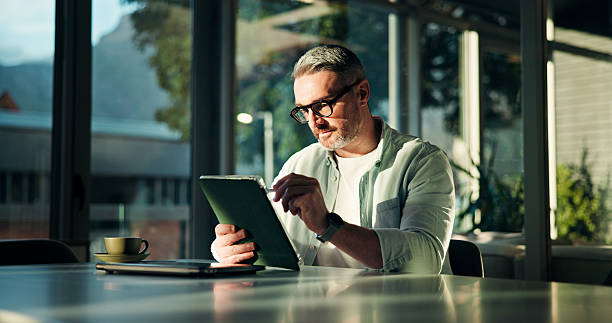 istock Business, tablet and man in office, internet and brand manager with email, network and browsing. Mature person, creative agency and employee in coffee shop, tech and kpi project with connection 2241294425