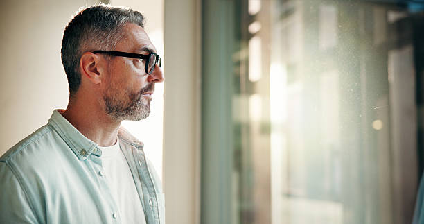 istock Businessman, serious and thinking by window in office for startup vision, business plan or ideas. Space, mature person or reflection at work for company development, funding solution or brainstorming 2241294442
