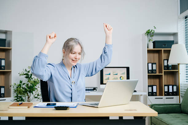 businesswoman celebrating success while analyzing reports in a modern office. Ideal for finance, accounting, achievement, statistics, and business growth themes.