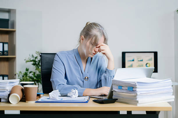 istock Exhausted businesswoman surrounded by documents and coffee cups, stressed from deadlines and workload. Ideal for burnout, corporate fatigue, and workplace pressure themes. 2241294729