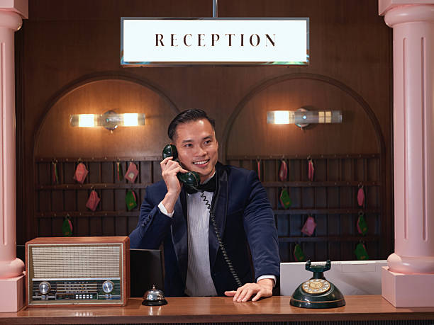 istock Smiling chinese hotel receptionist answering phone call at retro reception counter with vintage decor 2241306750
