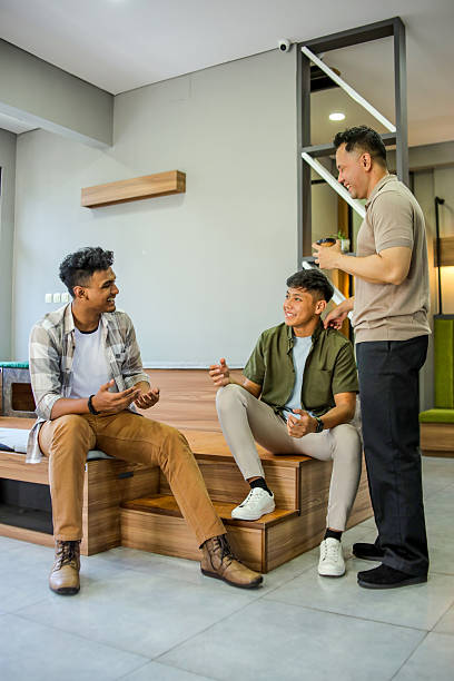 Three Diverse Men in Casual Attire Having Friendly Conversation While Standing and Sitting in Modern Indoor Space