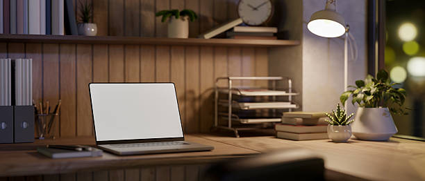istock Blank screen laptop and book under lamp light on wooden table in dim room or office, Work or Study. 2241308346