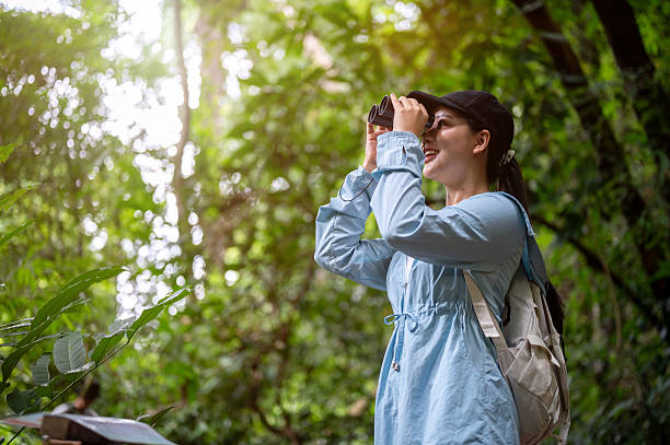 istock Pretty asian woman tourist smiling while looking through binoculars during forest hiking or trekking 2241308485
