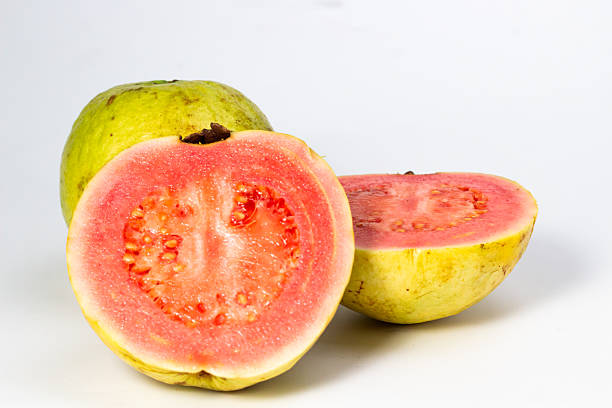 Fresh guava halves and a whole fruit display vibrant pink pulp against white background simplicity.