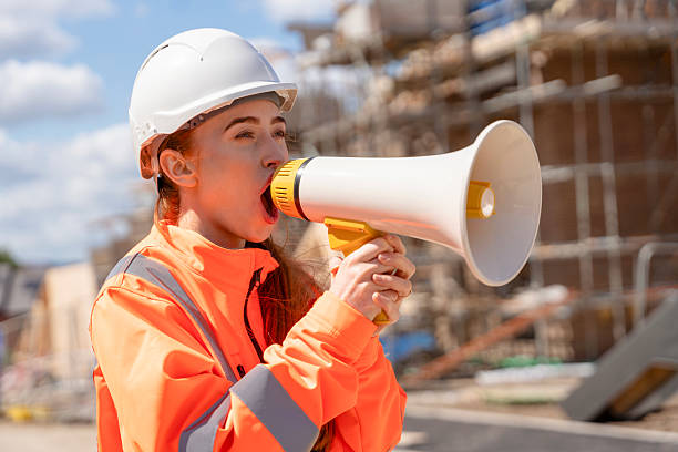 istock Builder woman girl in orange jacket screaming in megaphone loudspeacker on construction site to bring attention 2241316734