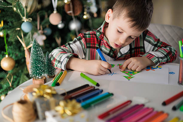 istock Boy Drawing Christmas Tree with Markers at Table Near Decorated Holiday Tree 2241320774