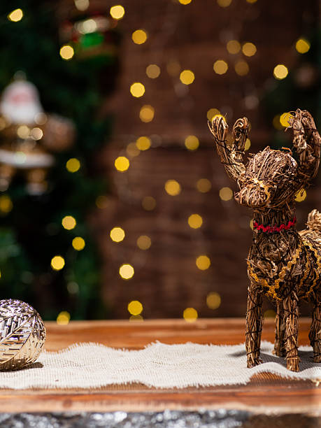A festive arrangement featuring a woven basket adorned with greenery, colorful Christmas ornaments, golden bells, and small wrapped gifts. The scene conveys a cheerful holiday spirit.